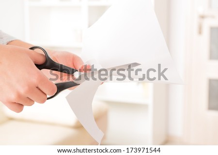 Woman\'s hands holding blank sheet of paper and cutting it with pair of scissors