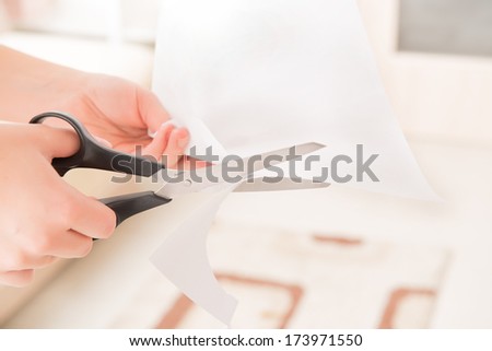 Woman\'s hands holding blank sheet of paper and cutting it with pair of scissors
