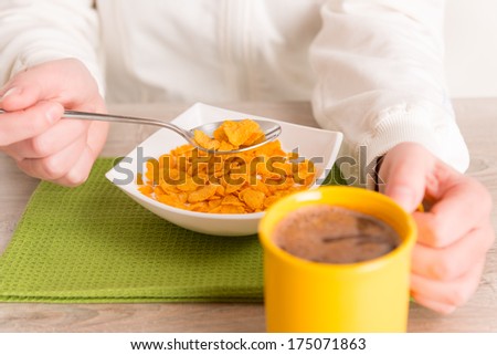 Woman\'s hands holding spoon over bowl full of cornflakes