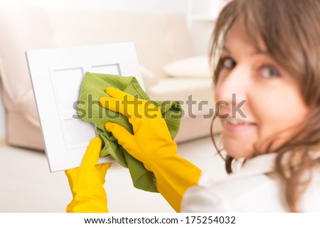 Beautiful young woman cleaning frame in her home wearing yellow gloves and using cloth