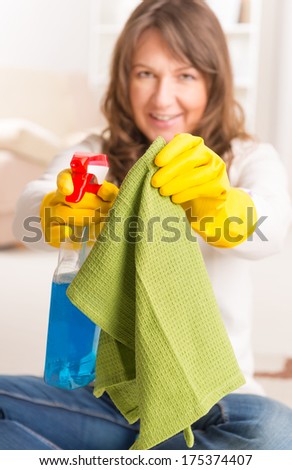 Beautiful young woman cleaning her house wearing yellow gloves with spray cleaners and cloth