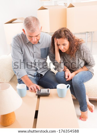 Mature couple at new home sitting and using calculator to sum their expenses and loans