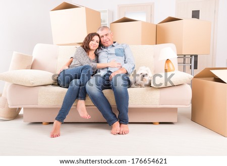 Happy mature couple celebrating their new home sitting together on the sofa with their little dog  just after moving in