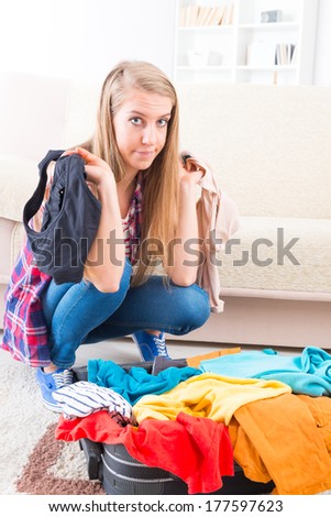 Young girl preparing her suitcase before travel. She is in doubt of what to pack