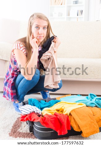 Young girl preparing her suitcase before travel. She is in doubt of what to pack