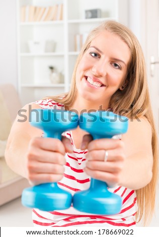 Young woman doing exercise with dumb bell, strengthen her arms and shoulders at home
