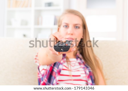 Young woman holding remote control and watching tv at home, focus on hand with remote