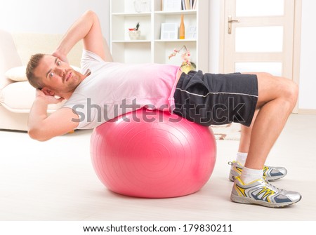 Happy attractive sporty handsome man doing sit ups exercises on the gym ball at home
