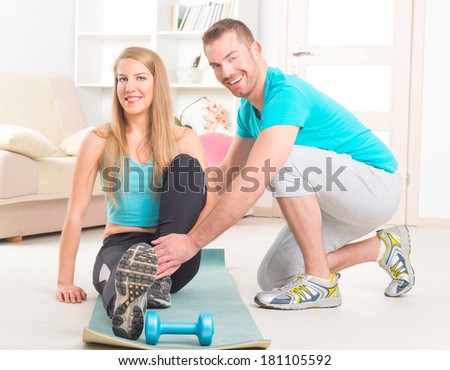 Beautiful young woman doing stretching exercises with personal trainer at home