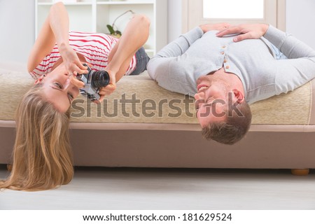 Young couple laying on the bed with heads upside down, woman taking picture with old analog camera