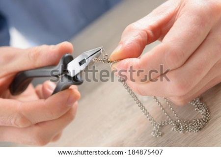 Man repairing or creating jewelry silver chain with pliers