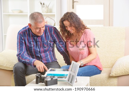 Cheerful couple looking at pictures on a photo album on the sofa at home