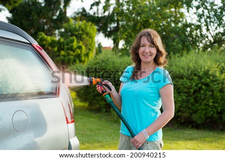 Woman washing her car in garden without detergents in ecological way.