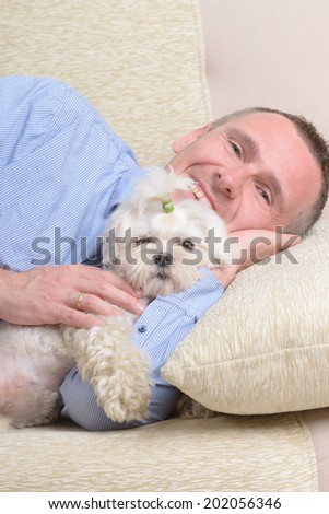 Little dog maltese resting with his owner on the sofa in home