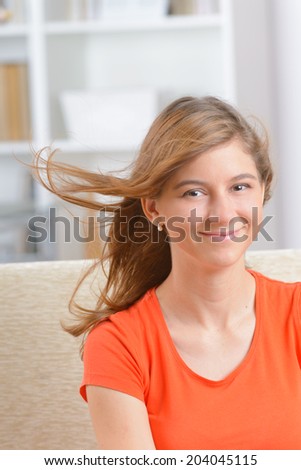 Cheerful yound woman sitting on sofa with wind in hair  in home and looking at the camera