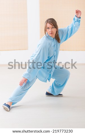 Beautiful woman doing qi gong tai chi exercise wearing professinal, oryginal chinese clothes at gym