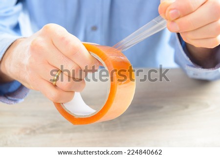 Hands with roll of transparent packaging, adhesive tape.