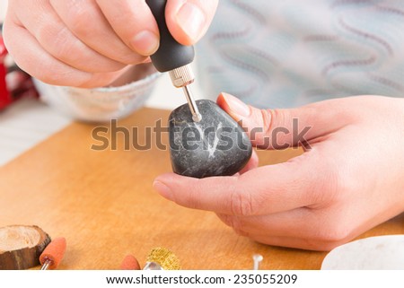Woman using a high speed rotary multi tool to engrave ornament on the stone
