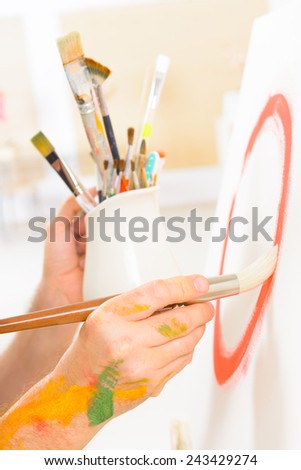 Hand holding paintbrush on canvas with other brushes in a background