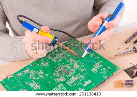 Serviceman soldering PCB with soldering iron in the service workshop