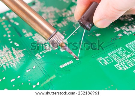 Serviceman soldering capacitor on PCB with soldering iron in the service workshop