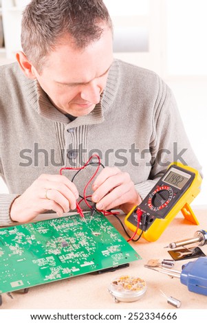 Serviceman checks PCB with a digital multimeter in the service workshop