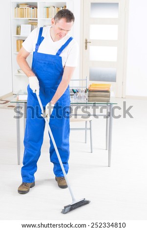 Smiling man cleaner standing with a broom at the office