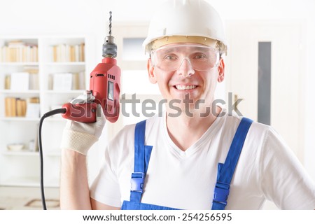 Smiling man with electric drill wearing protective helmet and glasses