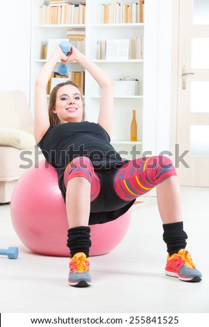 Young pregnant woman exercising with dumbbells and gym ball at home