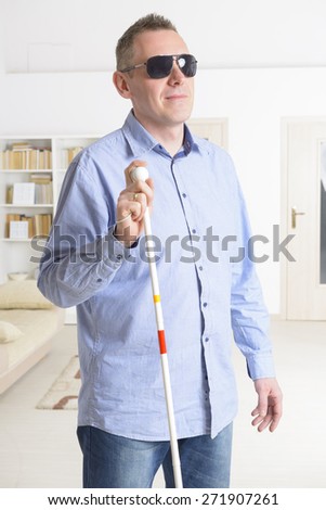 Blind man with white stick and dark glasses at home