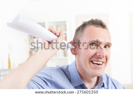 Man wearing deaf aid in ear attempting to hear something using paper tube