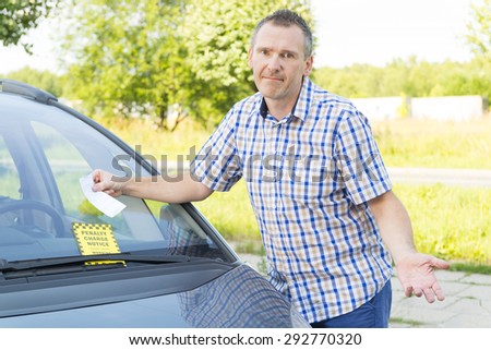 unhappy man looking on parking ticket placed under windshield wiper