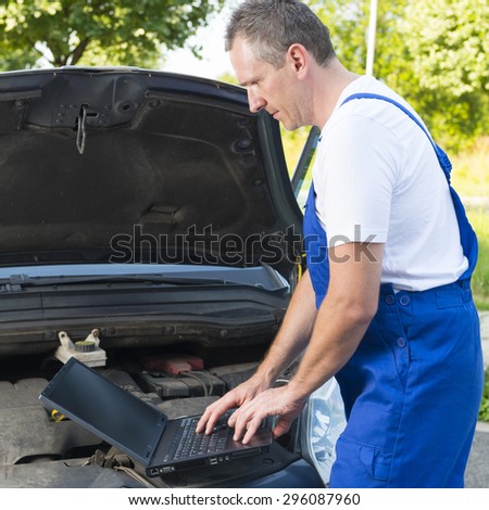 Mobile car service engineer checking car with his laptop on the road