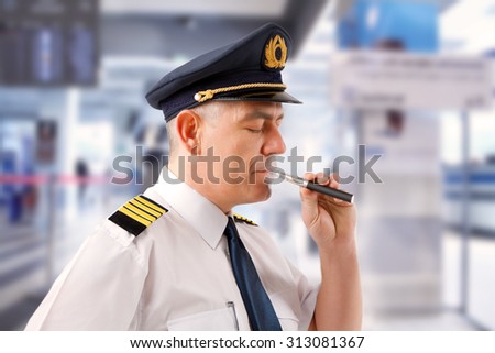 Airline pilot wearing uniform with epaulettes smoking electronic cigarette.