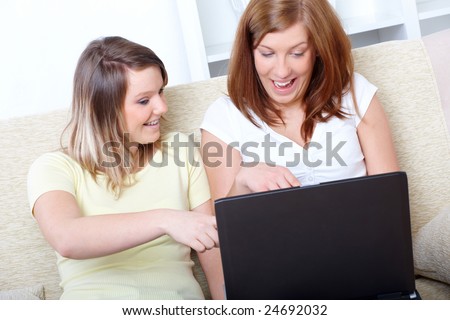 Two girls sitting on the sofa with laptop computer; one has got a brace