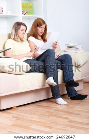 Two girls sitting on the sofa with paper notes and learning; one has got a brace