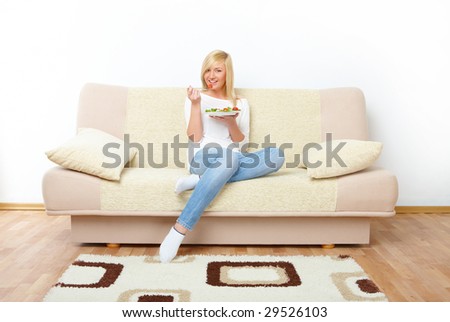 Beautiful woman sitting on the sofa and eating a healthy vegetable salad.