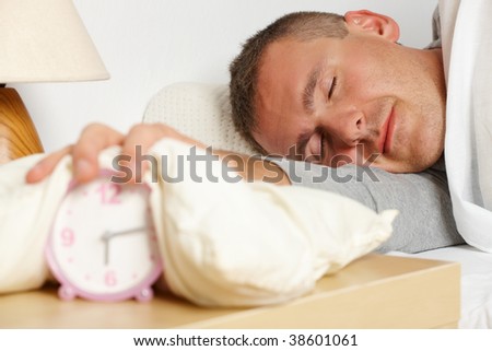 Sleeping man. His hand with pillow on the ringing clock showing morning.