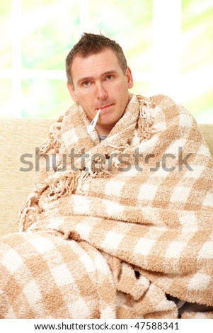 Man with cold sitting on sofa with thermometer in mouth