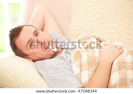 Man with cold laying on sofa with thermometer in mouth