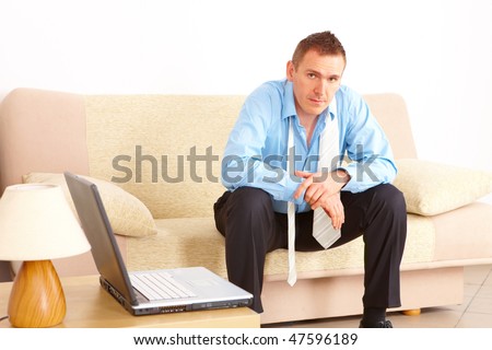 Tired businessman sitting on sofa after long day of work. Laptop computer on the left.