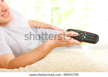 Relaxed man smiling lying on sofa with remote control handheld, watching television in home
