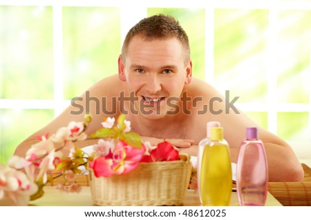 Man resting in sunny spa salon laying on the mat with flowers and cosmetics in foreground