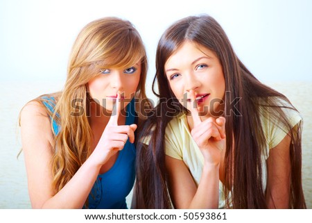 Two beautiful young girls gesturing for quiet with fingers over mouth shushing. Conceptual image illustrating secret or mystery