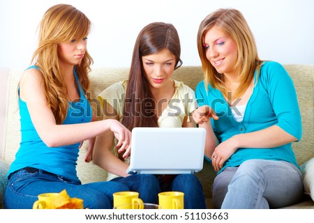 Three happy friends beautiful girls sitting on sofa in home with laptop computer