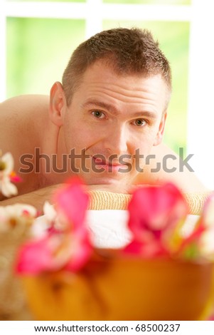 Man resting in sunny spa salon laying on the mat with flowers
