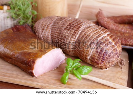 Natural prepared slow food smoked pork sirloin, cured pork shoulder which looks similar to ham and ring-shaped sausage in the background all on the wooden board with herbs