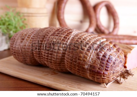 Natural prepared slow food cured pork shoulder which looks similar to ham, smoked pork sirloin, and ring-shaped sausage in the background all on the wooden board with herbs