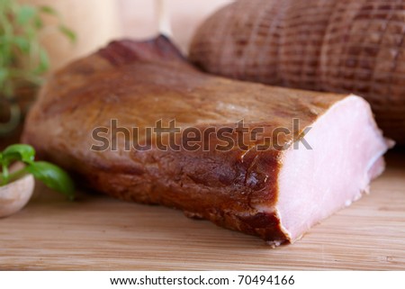 Natural prepared slow food smoked pork sirloin and cured pork shoulder which looks similar to ham in the background all on the wooden board with herbs