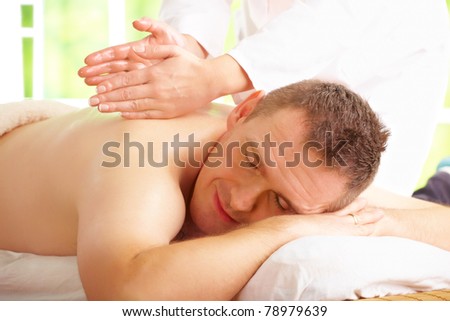 Man enjoying massage treatment with female hands on his back
